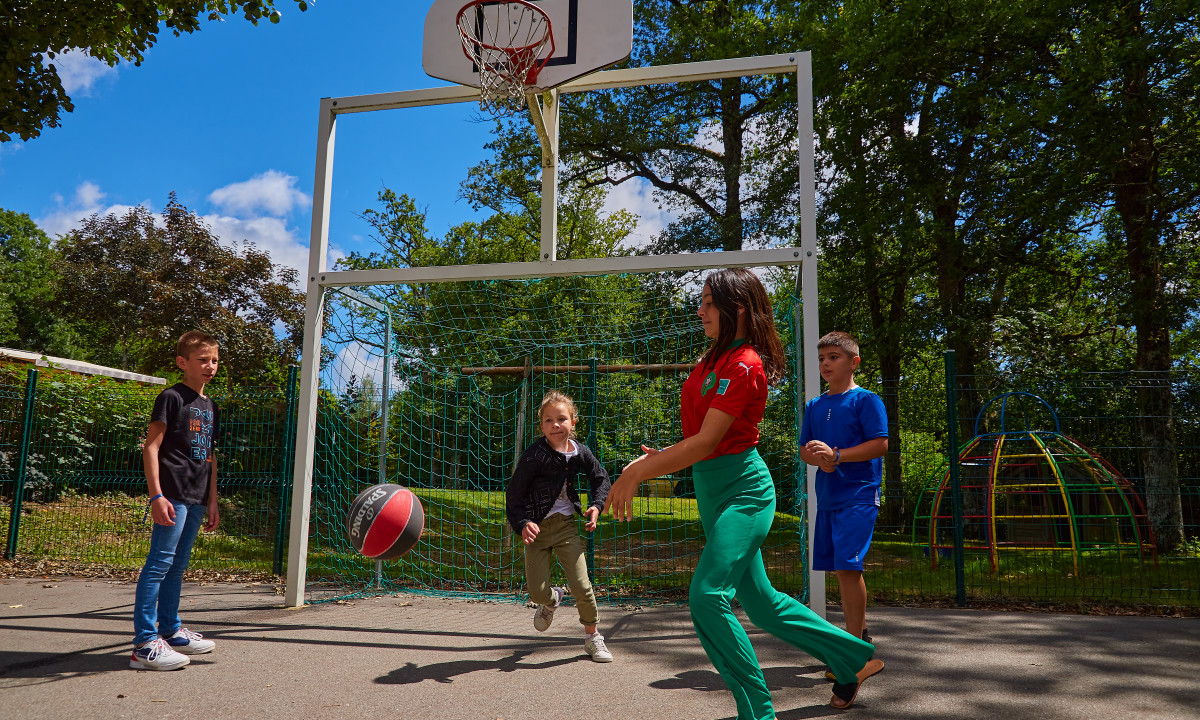 At Terrasses du Lac, four kids are playing basketball outside, with trees and a play structure in the background.