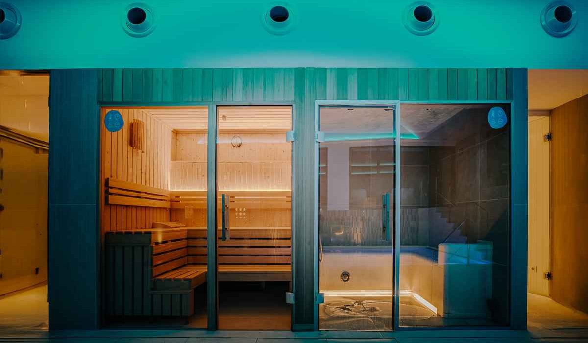 At Costa del Sol Glamping Village, a glass-enclosed sauna and a nearby hot tub are softly lit within a contemporary indoor wellness space.