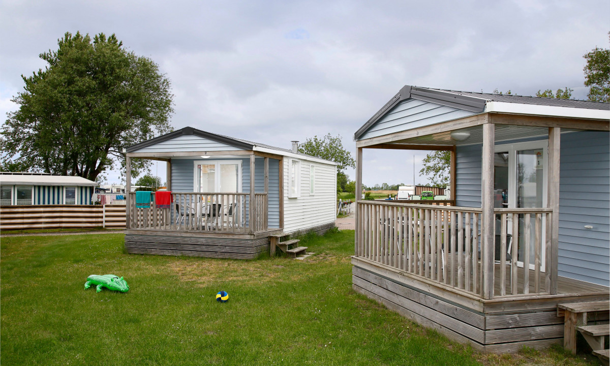 At KNAUS Campingpark Eckwarderhörne, mobile cabins with decks are situated on a grassy space, accompanied by toys and trees in the background.