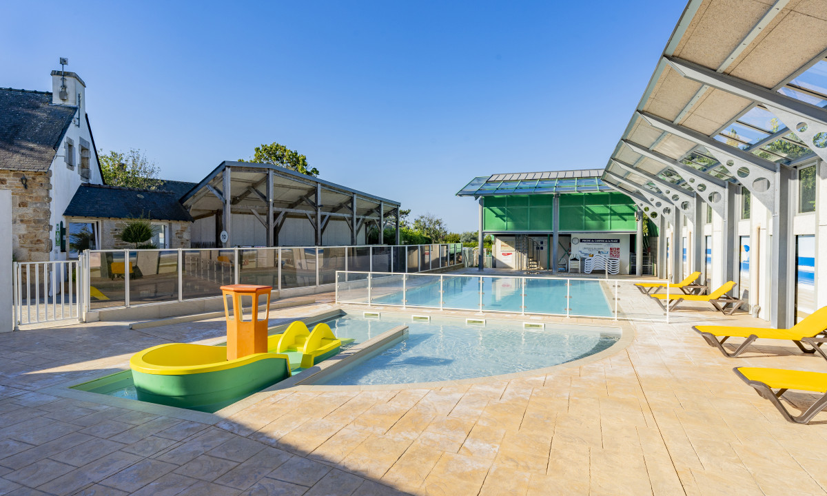 At De la Plage, a child-sized boat playground is situated in a poolside relaxation area featuring lounge chairs beneath clear skies.