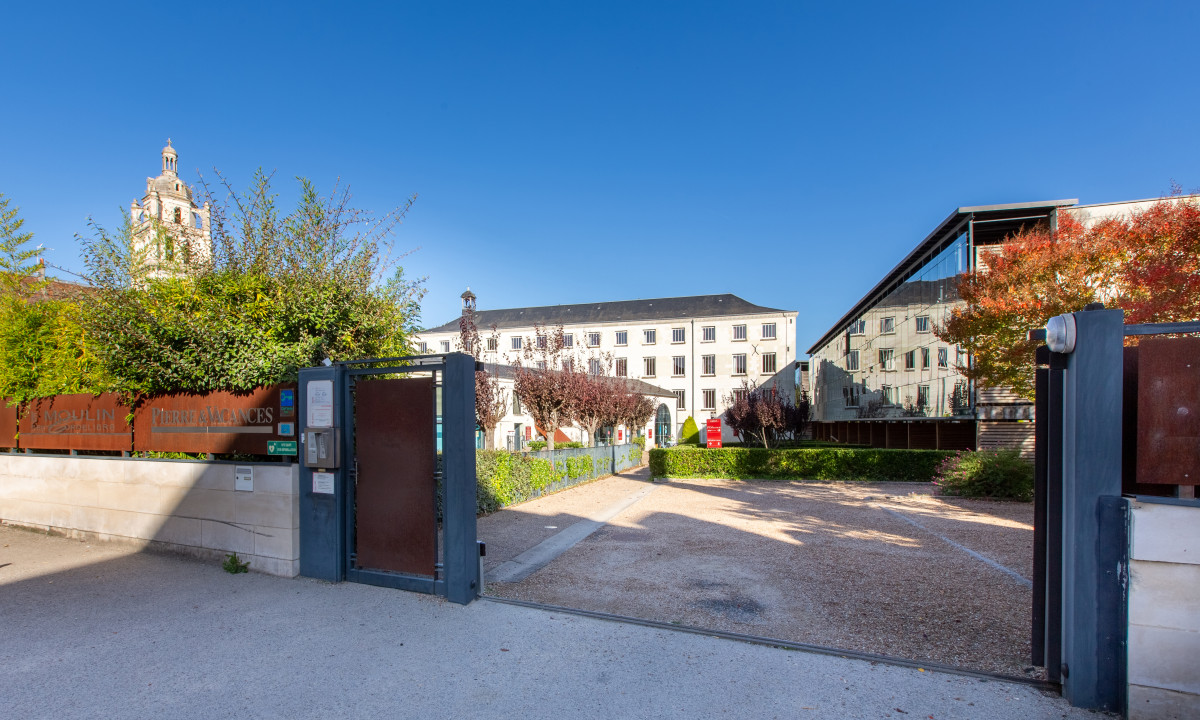 Gate entrance opened, revealing courtyard with garden and pathway, framed by historic buildings under clear blue sky at Le Moulin des Cordeliers
