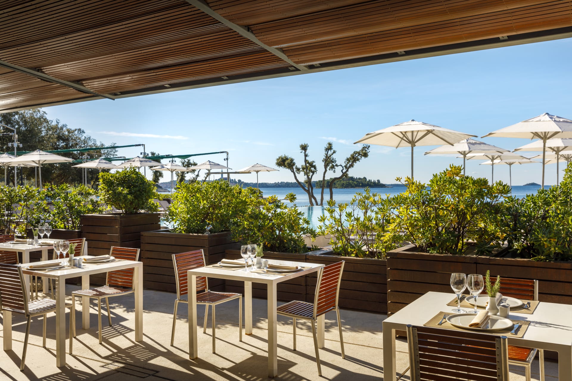 At Amarin, tables arranged for dining under a wooden shelter provide a view of vibrant foliage and a tranquil lake, with umbrellas visible nearby.