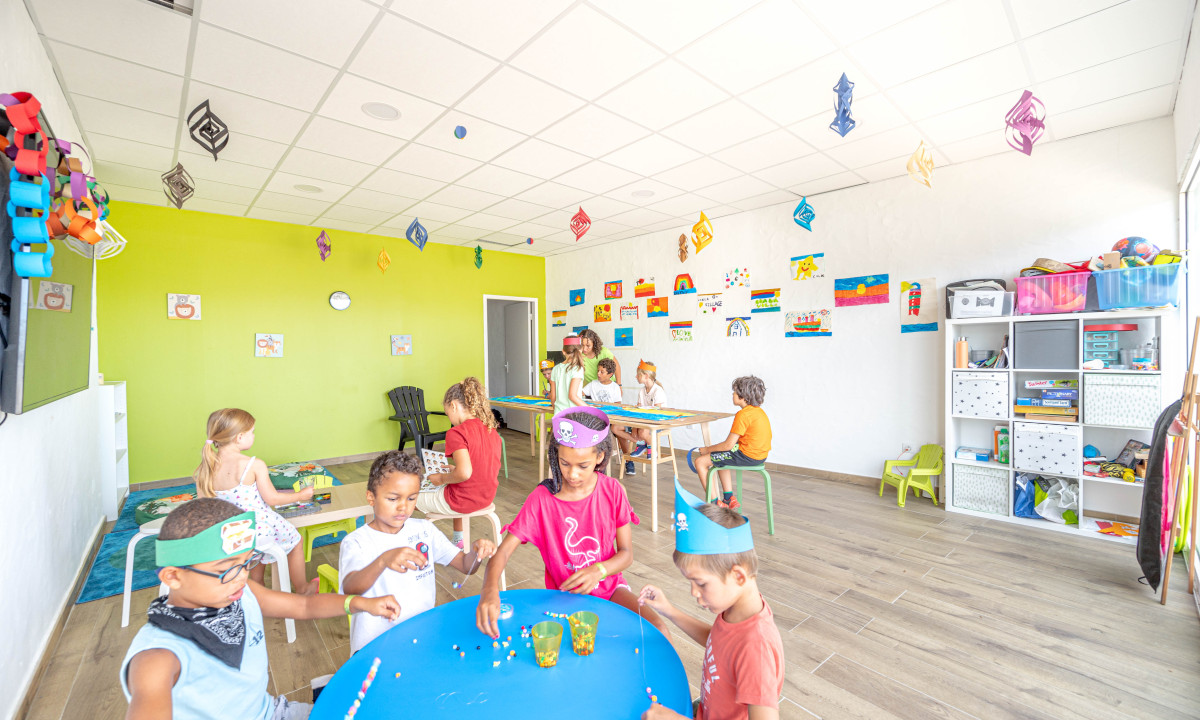 Children making crafts, seated at tables, in a brightly decorated classroom with artworks on the walls at Atlantica