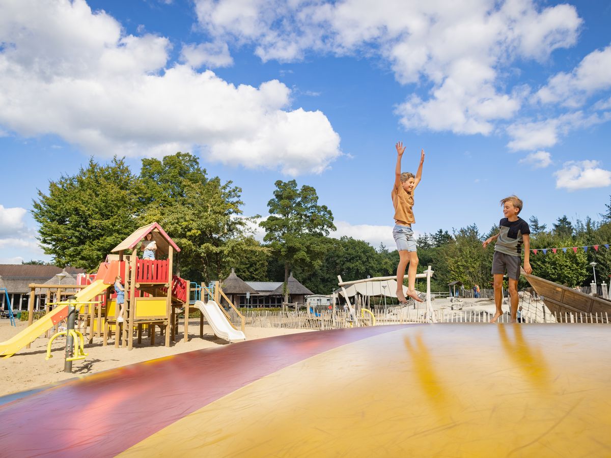 Children jumping on an inflatable cushion beside a colorful playground under a bright blue sky at Marvilla Parks Kaatsheuvel
