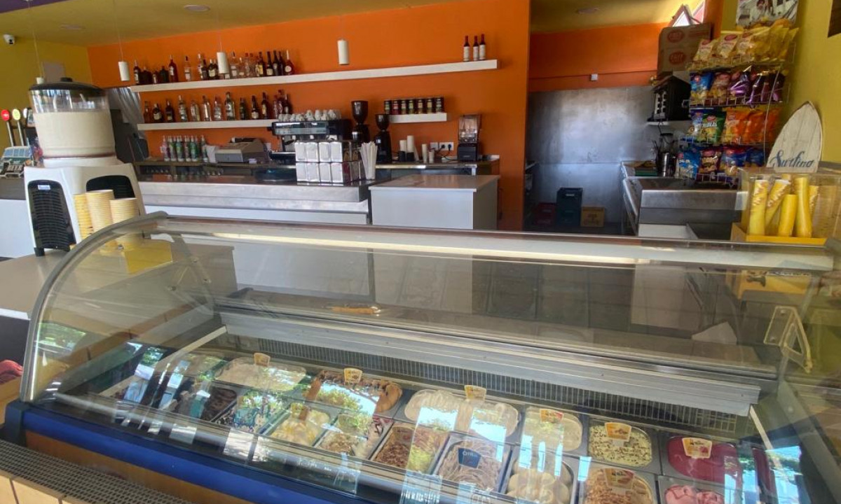 Ice cream counter displaying various flavors in a brightly colored café with shelves holding bottles and snacks at Resort Els Pins