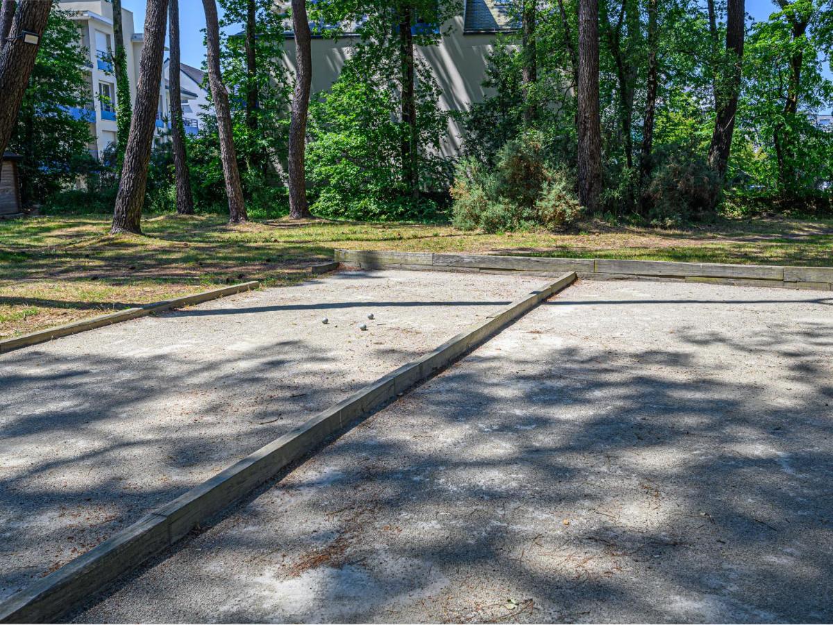 Wooden bocce ball court surrounded by trees and adjacent buildings at Ker Goh Lenn