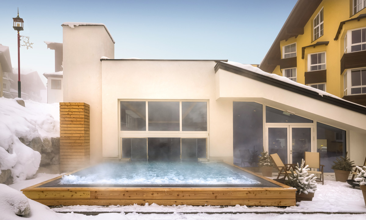 Steam rises from a hot tub surrounded by snow-covered ground near modern buildings at Valamar Obertauern Hotel