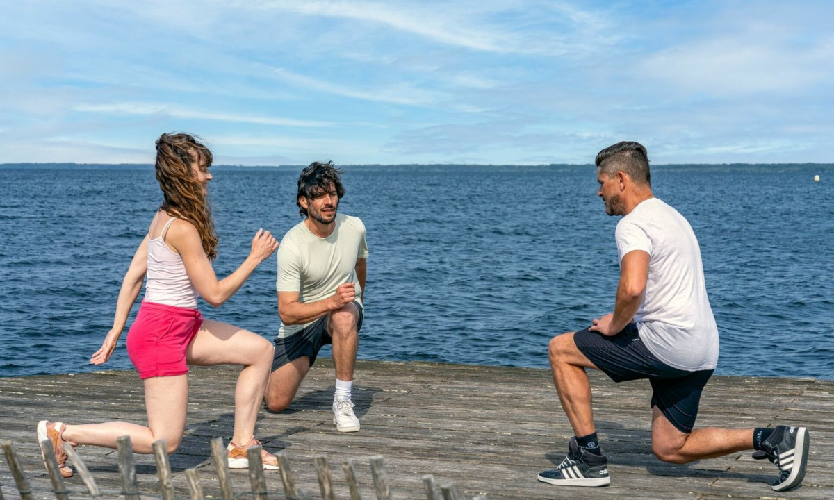 Three people lunging on a wooden pier beside a vast, calm lake under a clear blue sky at Maguide