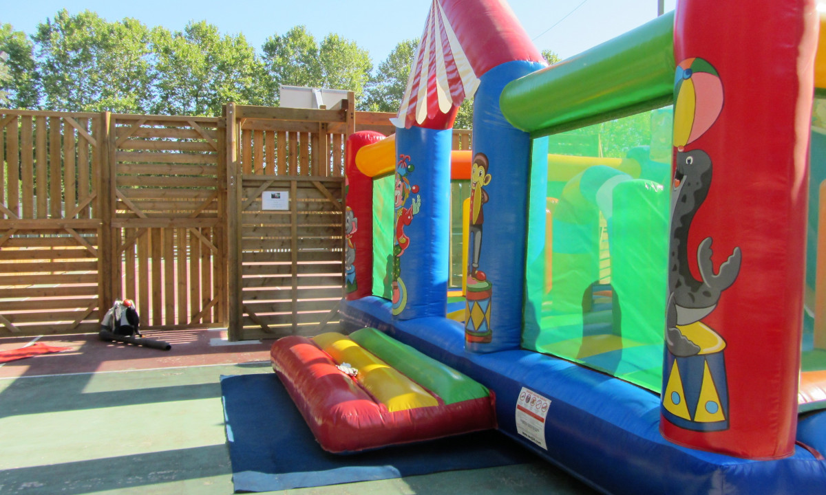 At La Clémentine, a vibrant inflatable castle is situated on a paved surface, enclosed by wooden barriers and trees in the backdrop.