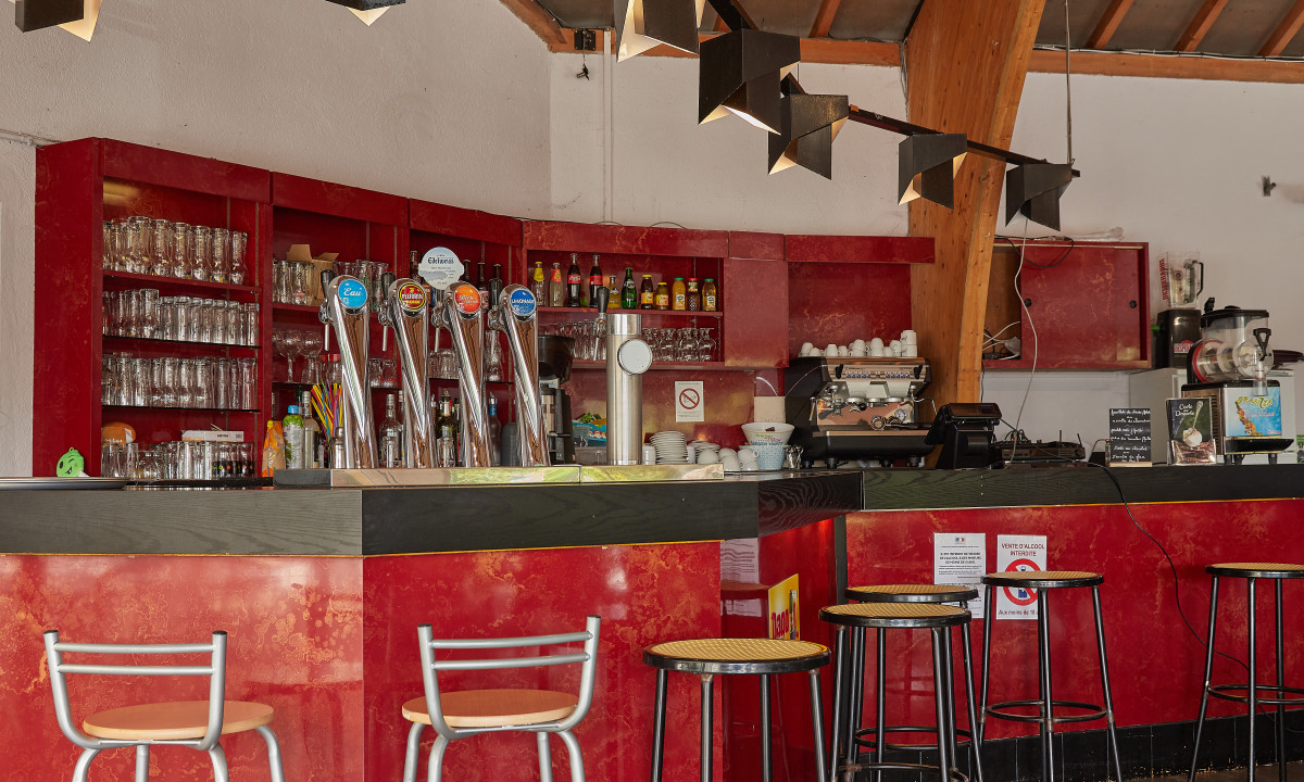 At Terrasses du Lac, a red bar counter showcases draft beer taps, seating stools, and glassware in a warm, contemporary bar setting.