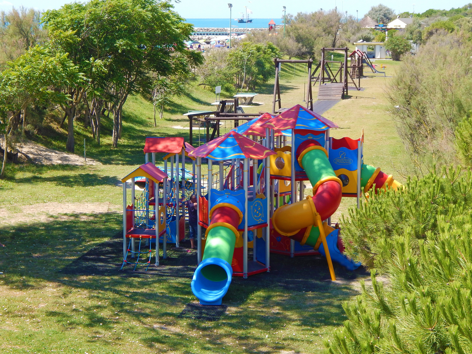 At Pra delle Torri, vibrant play structures featuring slides and climbing elements are nestled among trees and lush greenery.
