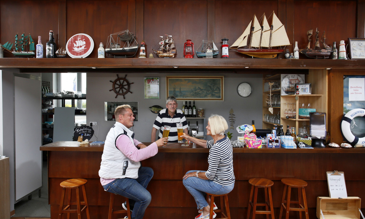 At KNAUS Campingpark Rügen, two individuals clink their beers together in a warm tavern decorated with miniature ships and maritime ornaments.