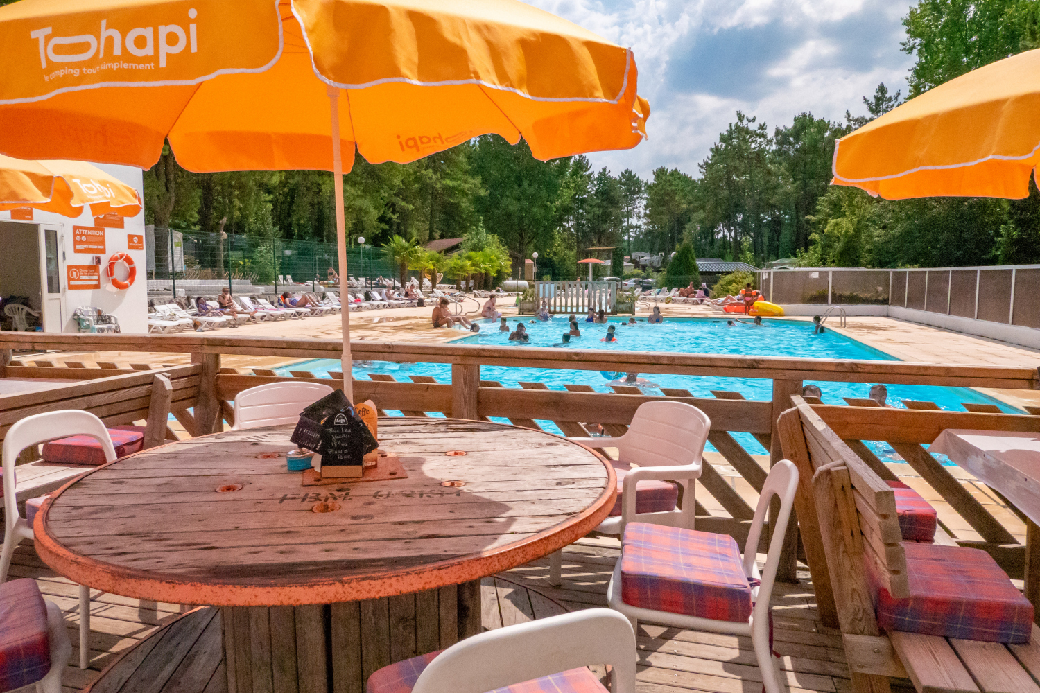 At La Dune Blanche, individuals are swimming in a spacious outdoor pool encircled by lounge chairs and shaded by orange umbrellas.