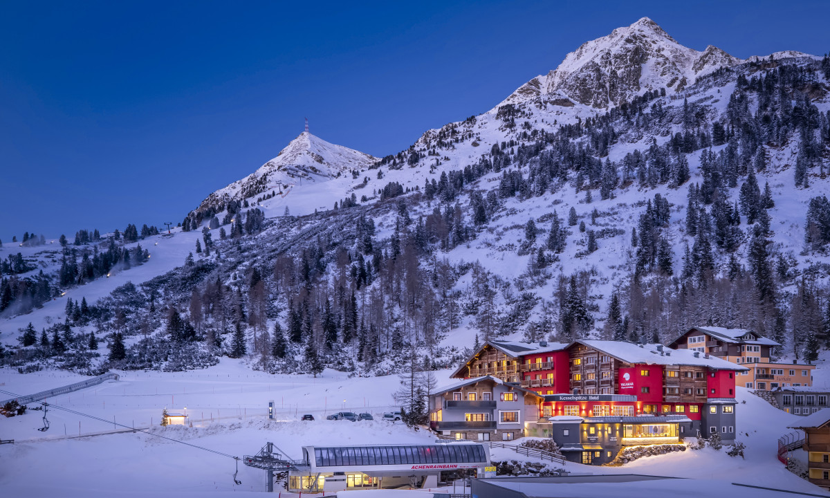 Snow-covered mountains surround a building with warm lights at twilight, creating a serene winter landscape at Kesselspitze Valamar Collection Hotel
