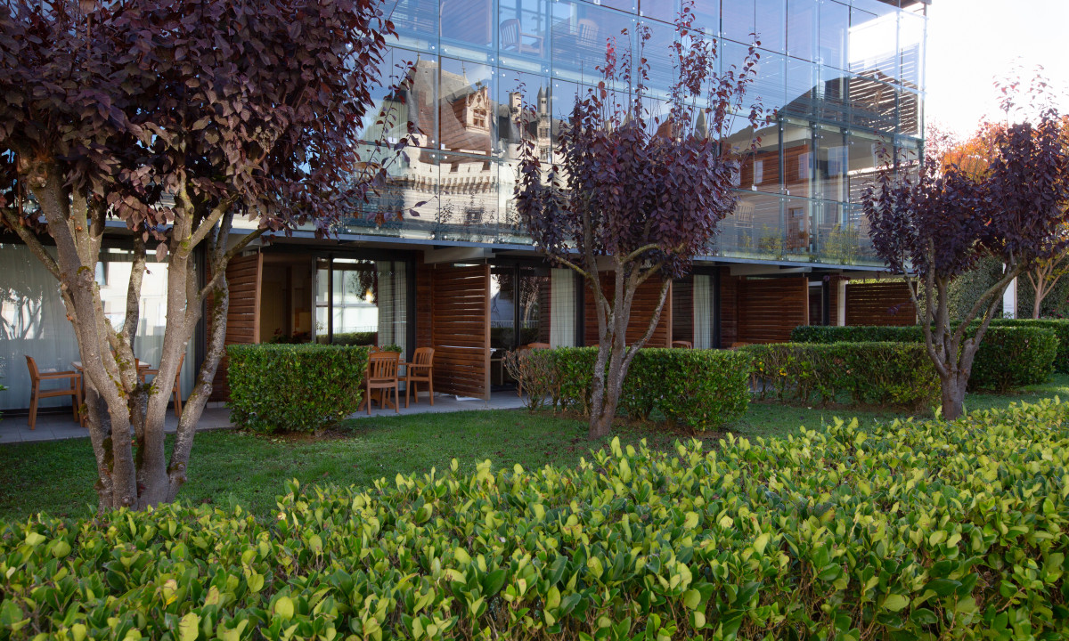 Building with large glass windows reflecting a castle, surrounded by green hedges and trees at Le Moulin des Cordeliers
