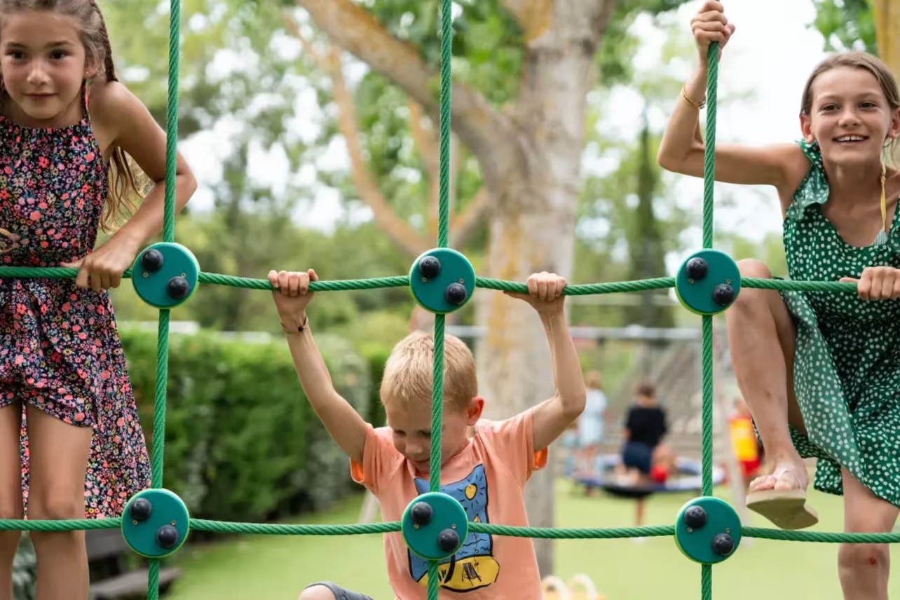 At Les Jardins de Tivoli, kids ascend a rope structure in a play area encircled by trees.