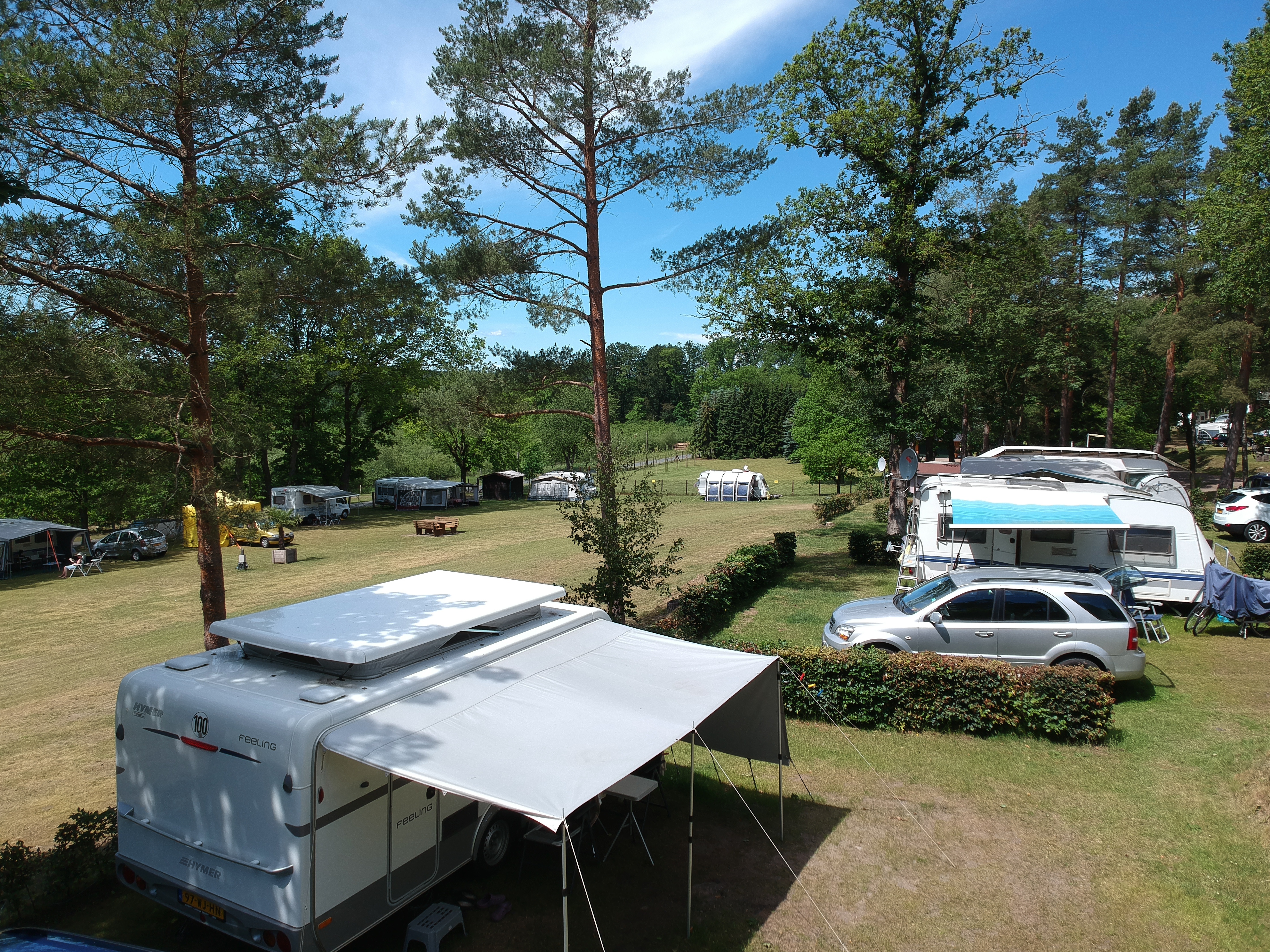 At Sonnenberg, a caravan is stationed with its awning extended, encircled by other caravans and tents on a grassy campsite beneath towering trees.