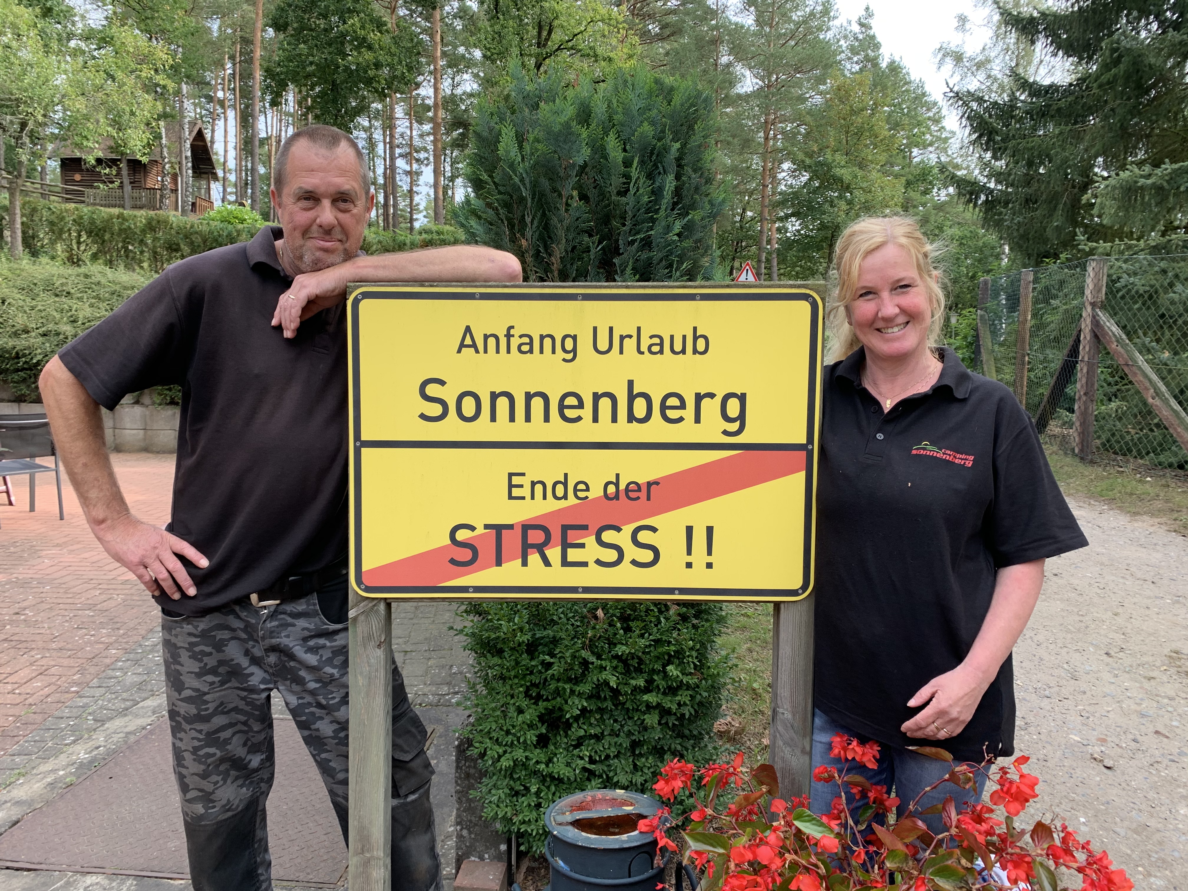At Sonnenberg, two individuals grinning and positioned next to a signpost in a forested region.