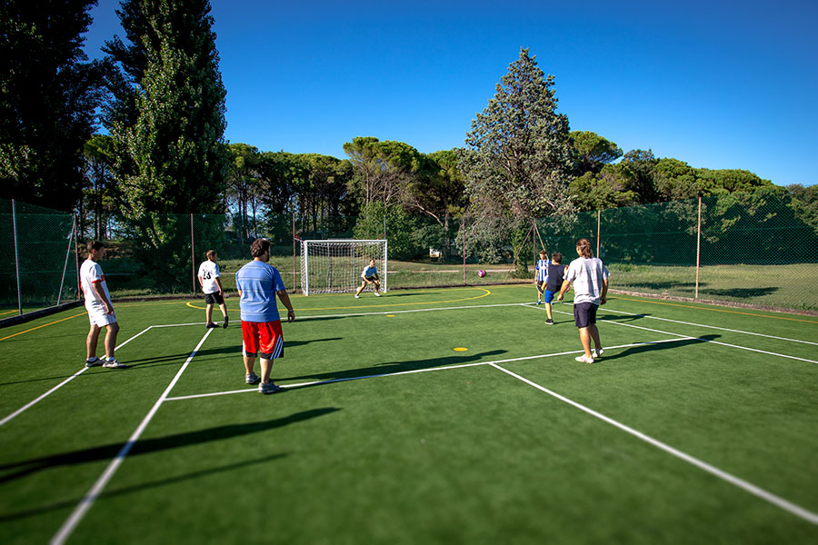 People playing soccer on a fenced outdoor field surrounded by trees at Belvedere Pineta