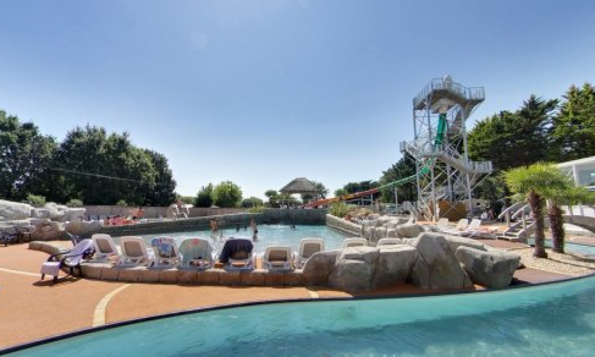 At Le Domaine de Léveno, a swimming pool is encircled by deck chairs and features a water slide tower, all set among trees.