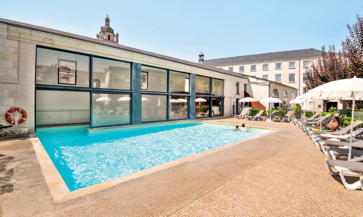 An outdoor swimming pool with people relaxing on lounge chairs and swimming beside a historic building at Le Moulin des Cordeliers