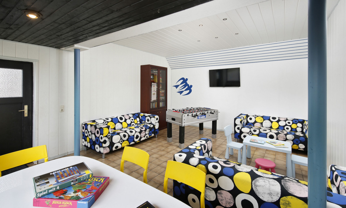 At KNAUS Campingpark Wingst, a foosball table and board games are placed on the table, encircled by patterned sofas in a leisure room.
