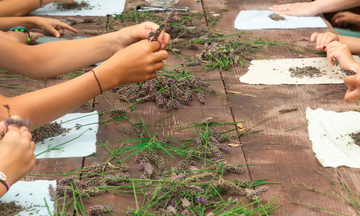 Hands sorting lavender and grass bundles on a rustic wooden table, surrounded by fabric squares at Domaine de Sévenier