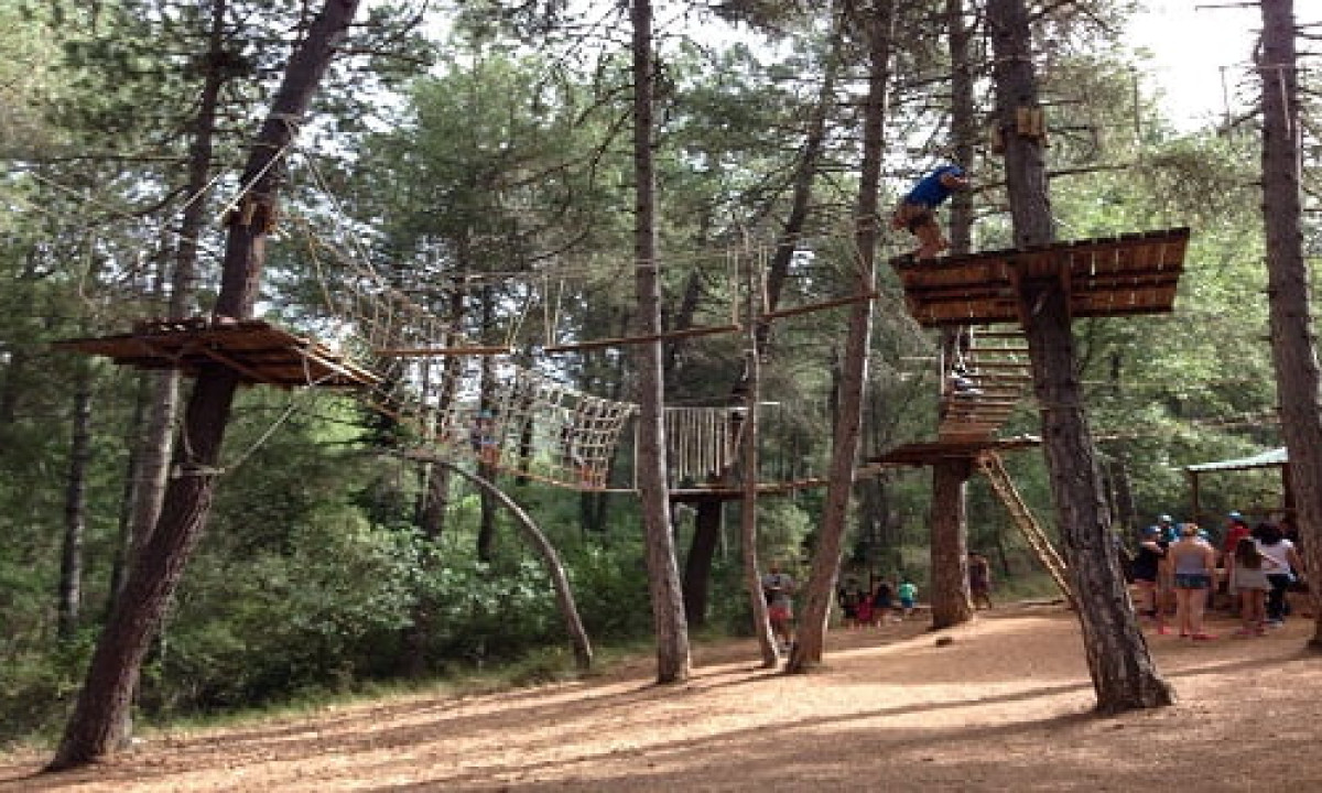 At Puente de las Herrerías, a high ropes course is elevated between trees with an individual ascending, while spectators observe from below in a forest environment.