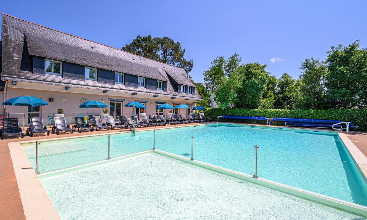 A large swimming pool with loungers and umbrellas beside a building in a green, sunny environment at Ker Goh Lenn