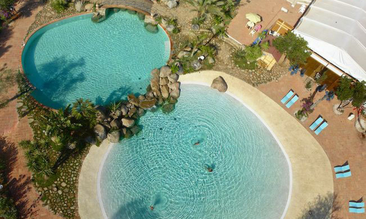 At Ultima Spiaggia, three linked swimming pools with swimmers are encircled by greenery, deck chairs, and a structure.