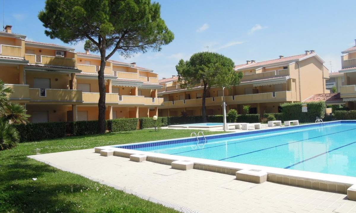 Swimming pool with metal ladders sits outdoors amidst green lawn, in front of beige multi-story buildings with balconies at Villaggio Selene