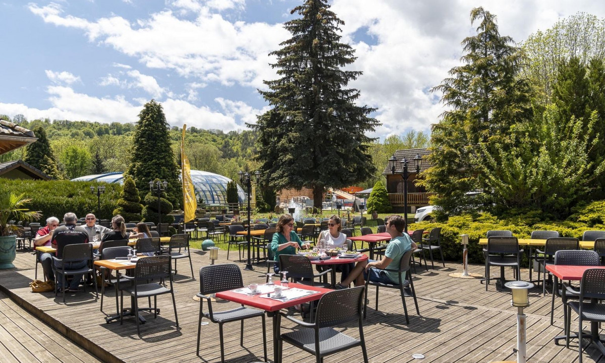 People dining on an outdoor wooden deck surrounded by trees and some structures at La Ribeyre