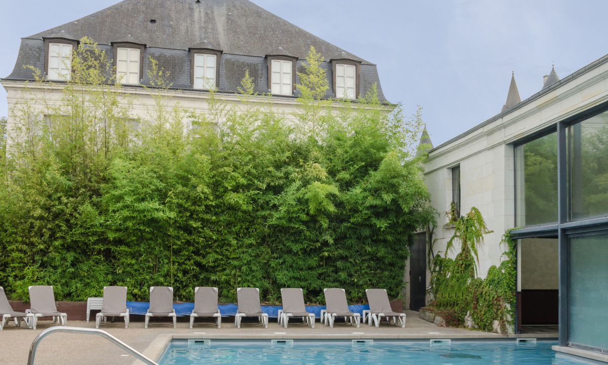 Pool surrounded by lounge chairs with a historic building and dense bamboo in the background at Le Moulin des Cordeliers