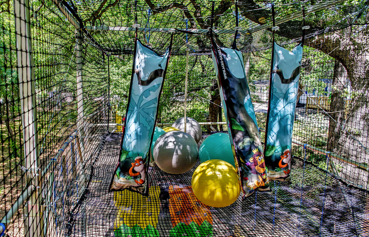 At Bois de Valmarie, vibrant play structures feature suspended punching bags and oversized balls enclosed by netting amidst the trees.
