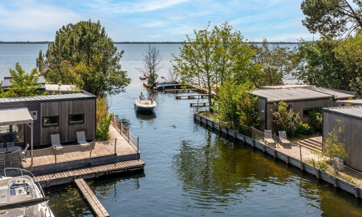 Boat cruising through a canal surrounded by modern wooden cabins and lush greenery at Maguide