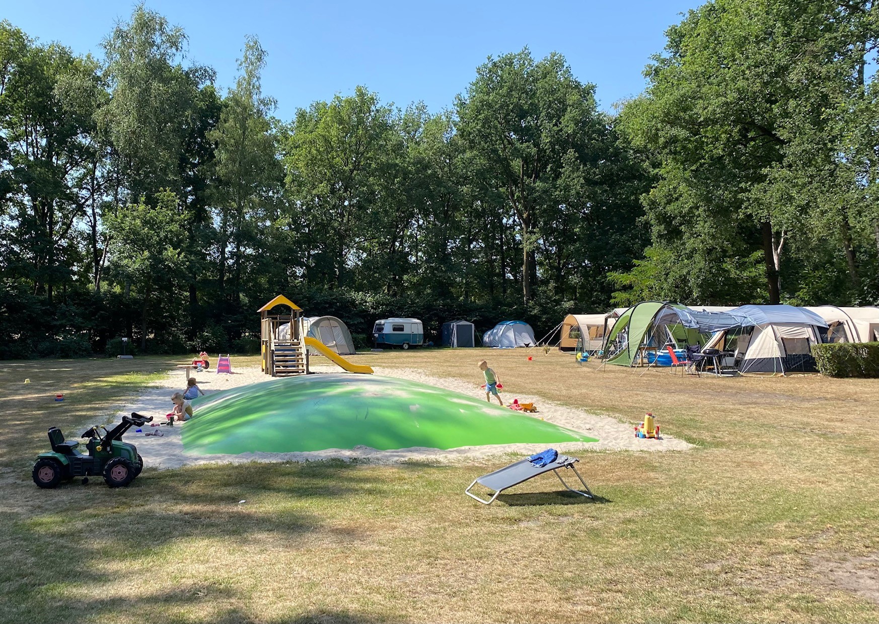 At de Vinkenkamp, kids are enjoying themselves on a vibrant elastic ground next to a modest play area and tents surrounded by towering trees.