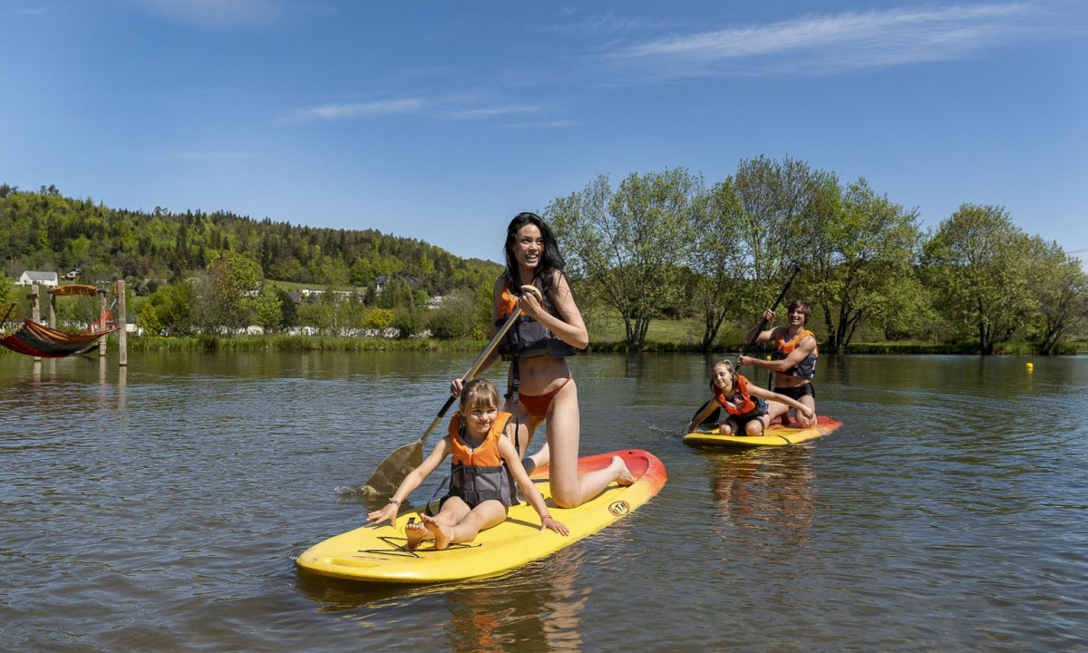 People paddleboarding on a calm lake near a green forested area with a hammock in the background at La Ribeyre