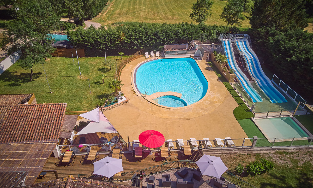At Le Chêne Vert, a swimming pool and water slides are encircled by lounge chairs and umbrellas, all set within a spacious, green campground environment.