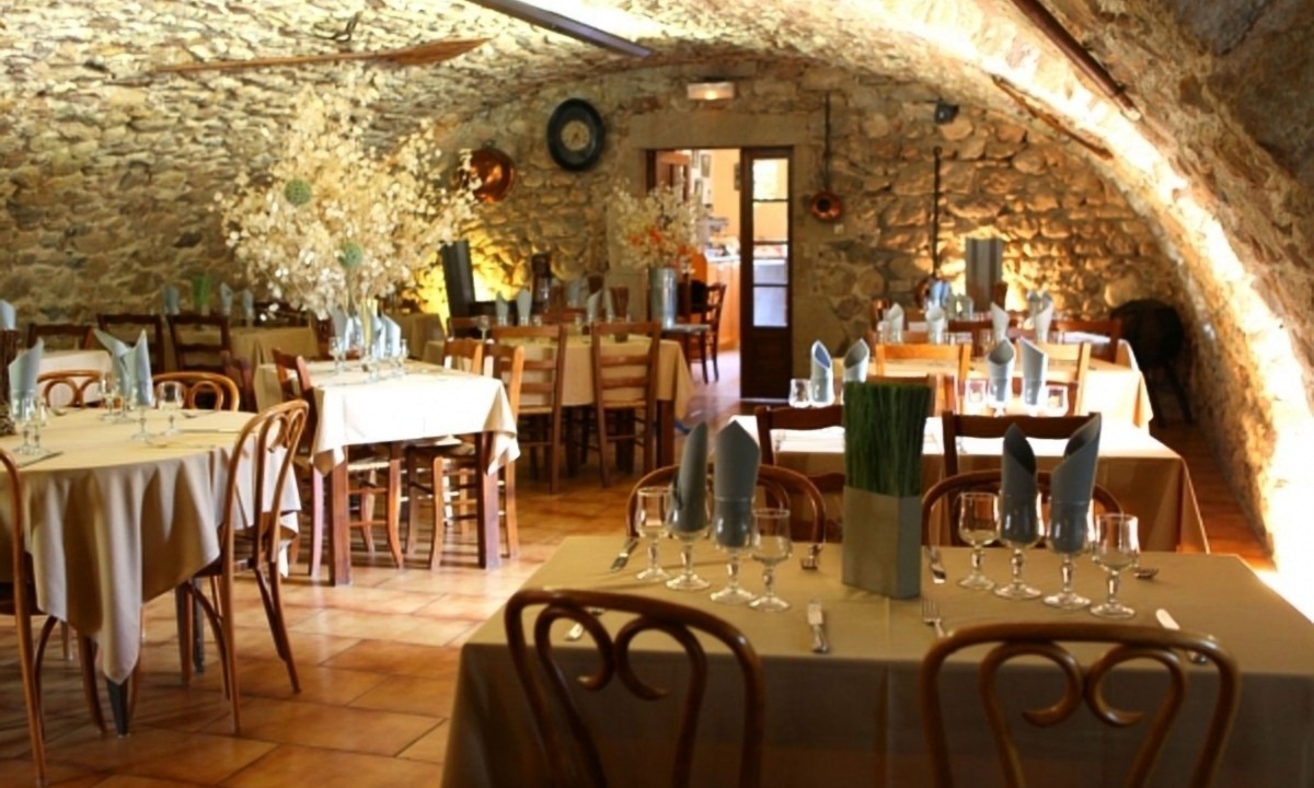 At Les Ranchisses, tables arranged with cloths and drinkware are found in a charming dining area featuring stone walls and vaulted ceilings.