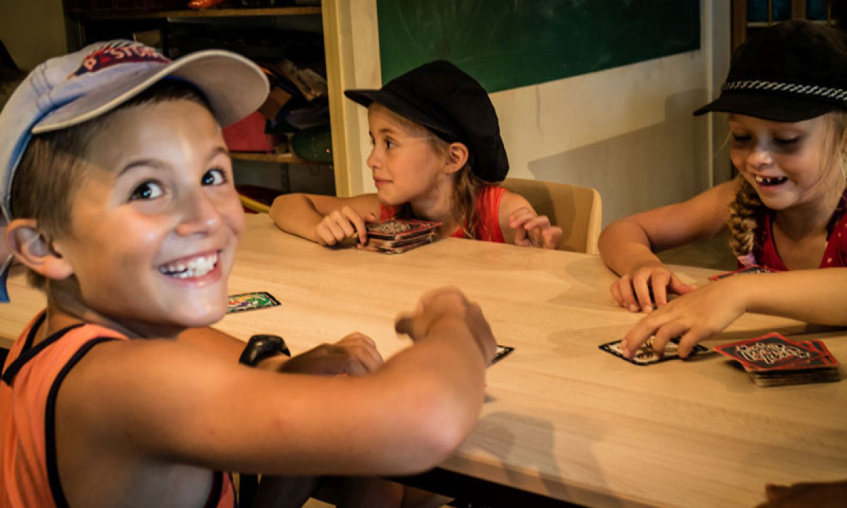 At La Sousta, three kids are engaged in card games around a table indoors.