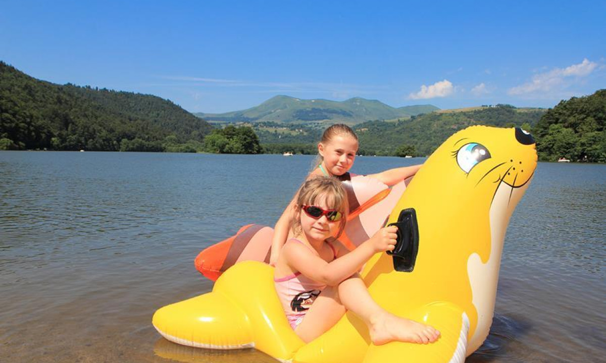 Two children on an inflatable seal in a lake with mountains and trees in the background at Paradis l'Europe