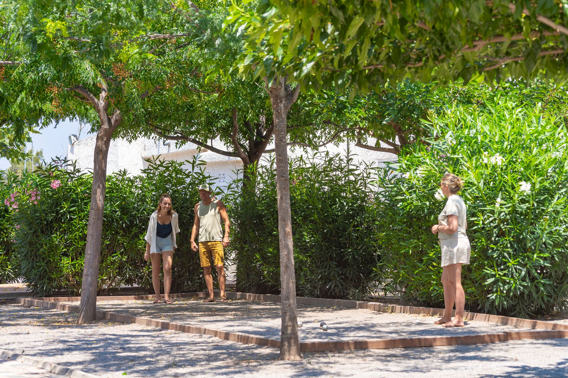 At Valencia, three individuals are playing pétanque, encircled by vibrant foliage and trees on a bright day.