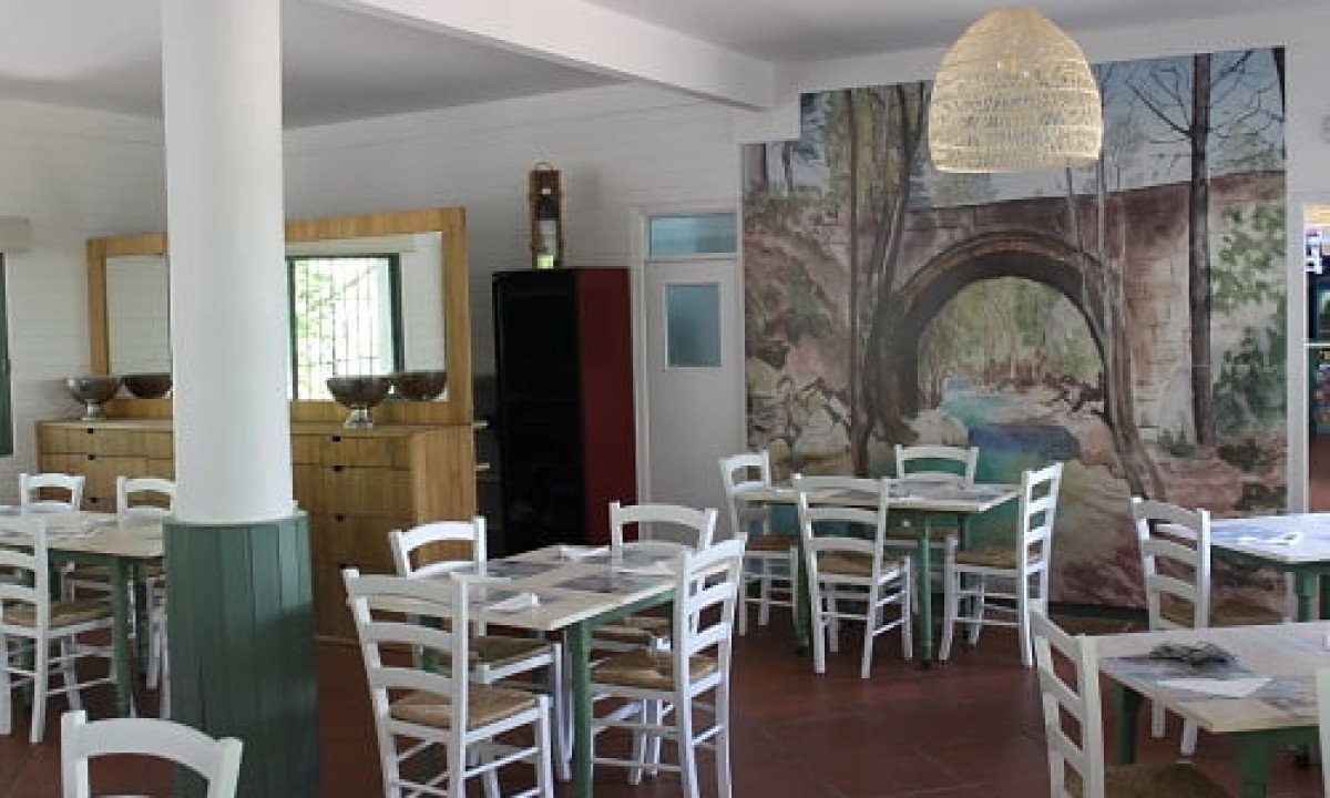At Puente de las Herrerías at the front, tables with light-colored chairs are set up in a warm dining area adorned with a mural depicting a stone bridge.