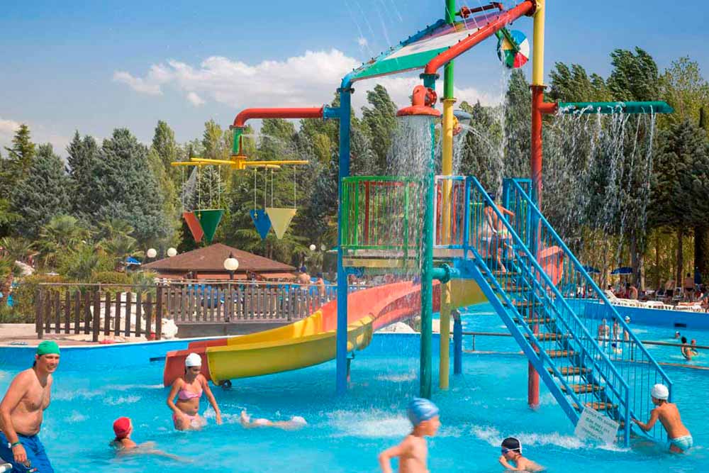Children playing in a colorful water playground with slides and fountains at Centro Vacanze Verde Azzurro