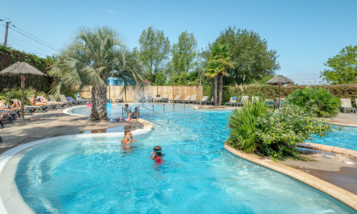 Children swimming in a pool surrounded by palm trees and lounge chairs at Atlantica