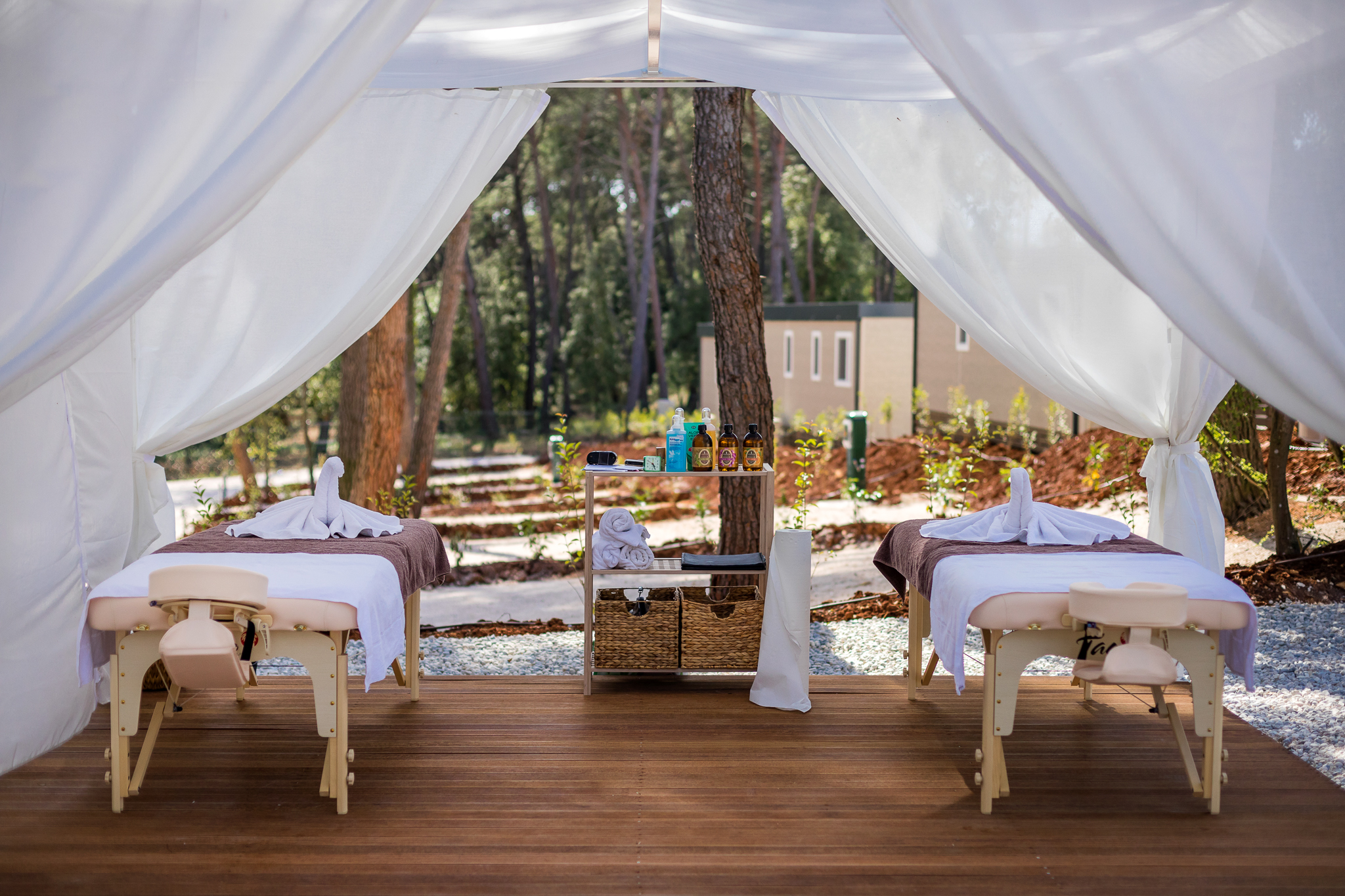 Massage tables with towels are set up inside a white tent, surrounded by trees and a building at Santa Marina Boutique