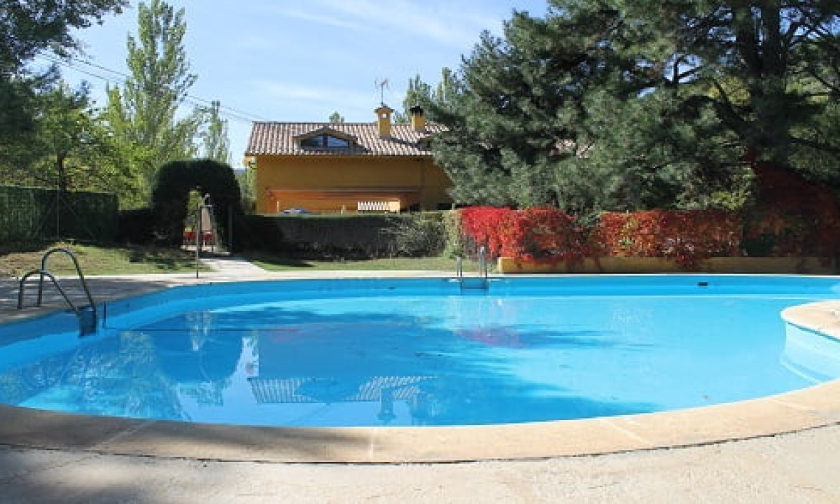 At Puente de las Herrerías, a pristine swimming pool mirrors the trees and a yellow structure, featuring ladders rising from the water, encircled by lush vegetation.