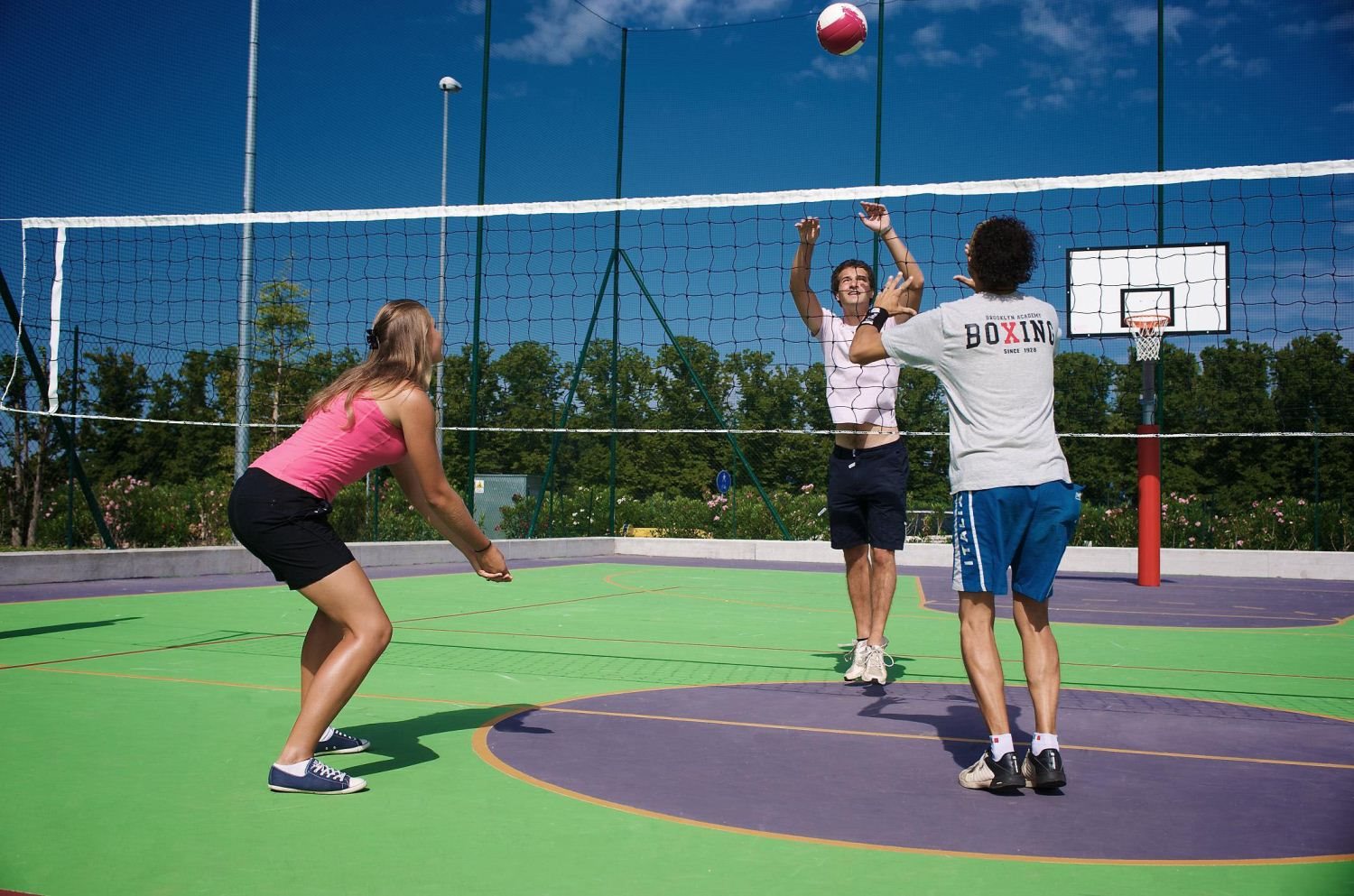 Three people play volleyball on an outdoor court beneath a clear blue sky at San Francesco