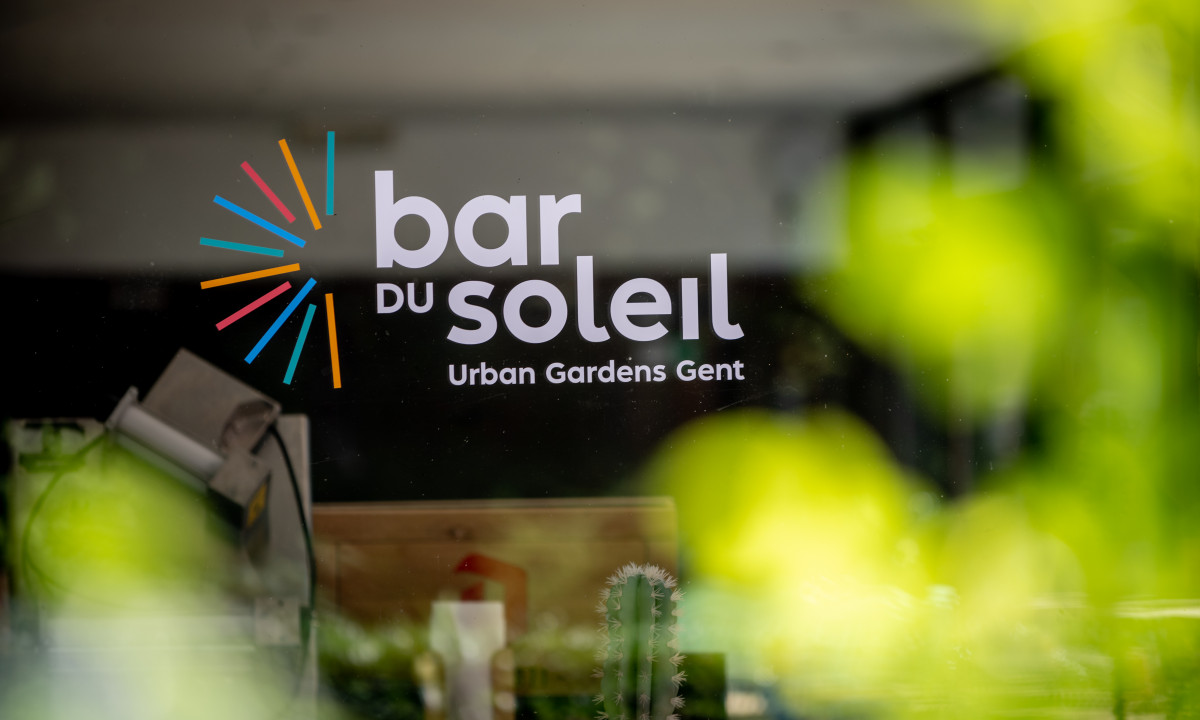 At Urban Gardens Gent, a sign reading "bar du soleil" is visible through vibrant rays and leafy foliage.