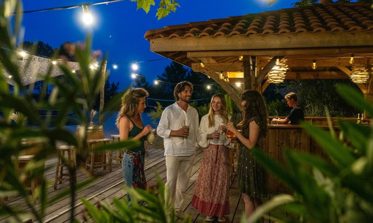 People socializing outdoors under string lights, near a wooden bar, surrounded by plants at Maguide